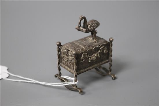 An early 20th century continental white metal novelty box and cover, modelled as a stork with baby upon a cradle,